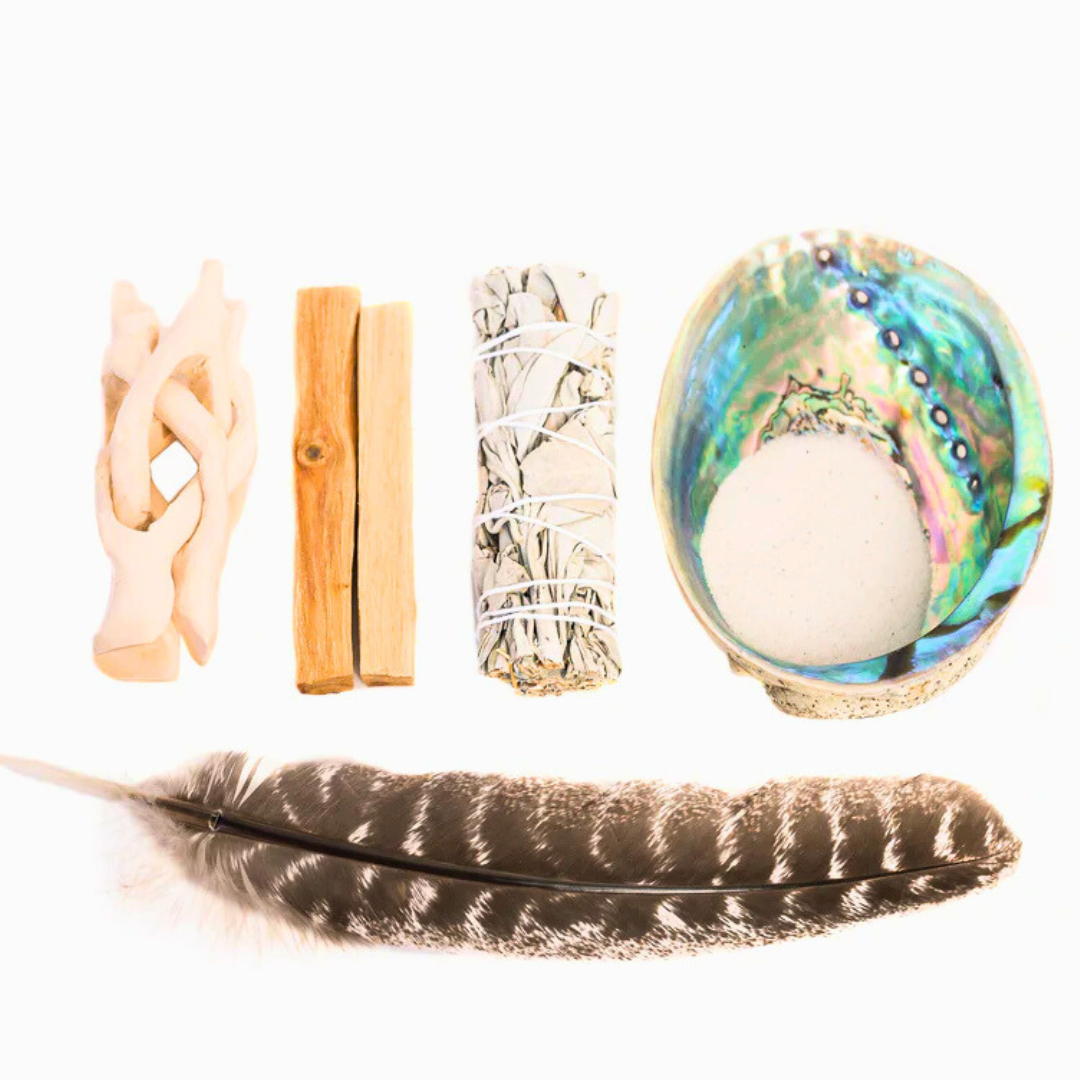 Collection of spiritual items including a White sage, feather, shell, and other objects on a white background